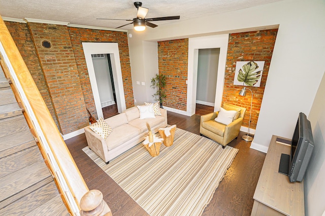 living area featuring a textured ceiling, brick wall, dark wood-type flooring, a ceiling fan, and baseboards