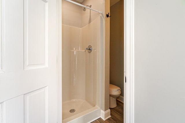 full bath featuring toilet, a stall shower, and wood finished floors