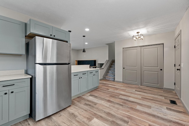 kitchen with light hardwood / wood-style flooring, stainless steel fridge, a textured ceiling, and decorative light fixtures