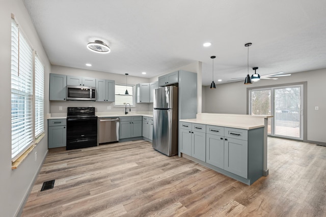 kitchen featuring pendant lighting, gray cabinetry, kitchen peninsula, stainless steel appliances, and light wood-type flooring