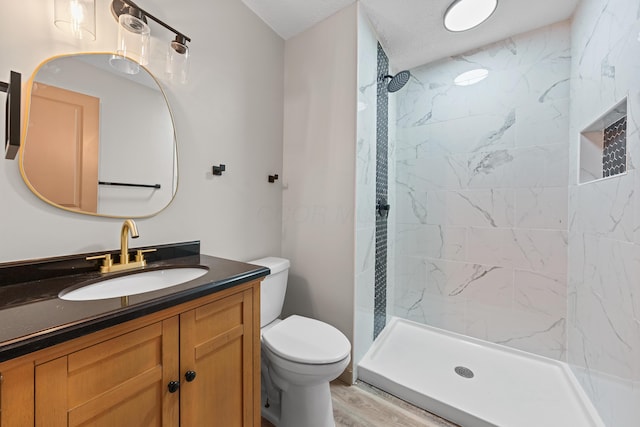 bathroom featuring hardwood / wood-style flooring, vanity, a tile shower, and toilet