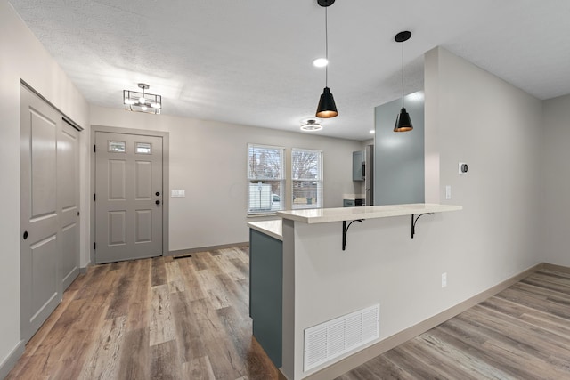 kitchen with a textured ceiling, hardwood / wood-style flooring, a kitchen breakfast bar, kitchen peninsula, and pendant lighting