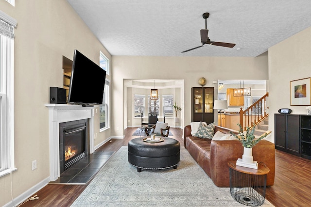 living room with a tiled fireplace, ceiling fan, dark wood-type flooring, and a textured ceiling