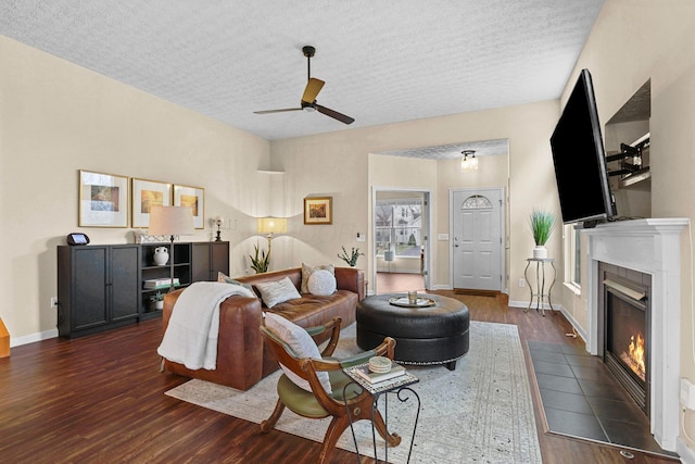 living room with ceiling fan, a textured ceiling, a fireplace, and dark hardwood / wood-style flooring