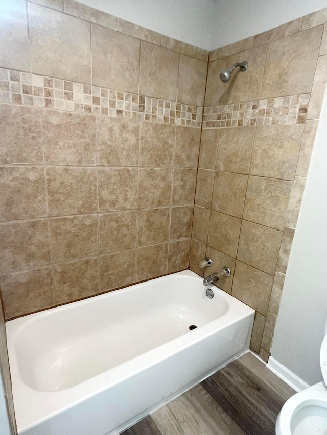 bathroom with hardwood / wood-style flooring, tiled shower / bath, and toilet