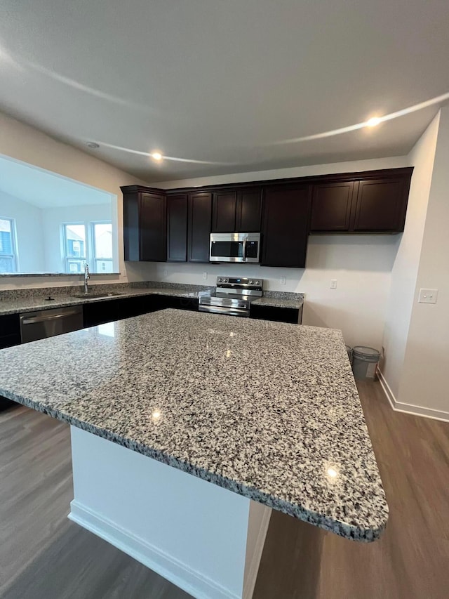 kitchen with sink, stainless steel appliances, dark hardwood / wood-style floors, light stone countertops, and a kitchen island