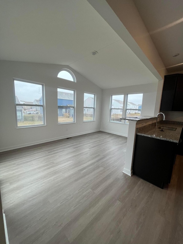 unfurnished living room featuring sink, vaulted ceiling, and light hardwood / wood-style floors