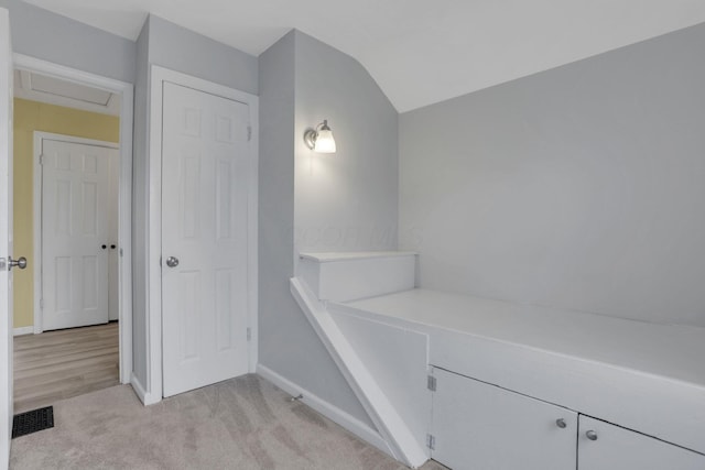 corridor featuring visible vents, baseboards, vaulted ceiling, and light colored carpet