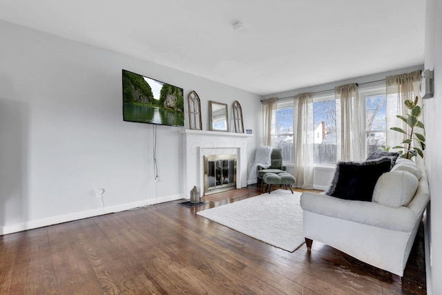 living room featuring a fireplace with flush hearth, baseboards, and wood finished floors