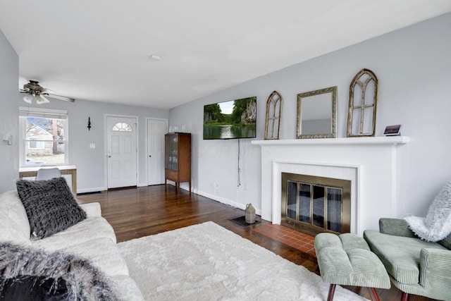 living area with lofted ceiling, a fireplace with flush hearth, baseboards, and wood finished floors