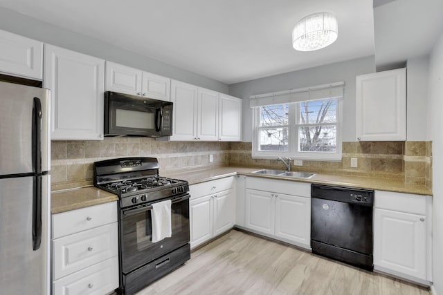 kitchen featuring white cabinets, decorative backsplash, light countertops, black appliances, and a sink