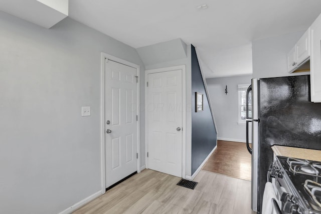 kitchen featuring light wood finished floors, baseboards, visible vents, stainless steel range with gas cooktop, and white cabinetry