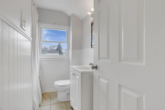 bathroom with tile patterned flooring, toilet, vanity, vaulted ceiling, and wainscoting