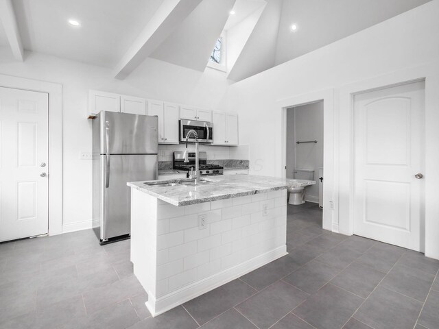 kitchen with white cabinetry, tasteful backsplash, light stone counters, a center island with sink, and stainless steel appliances