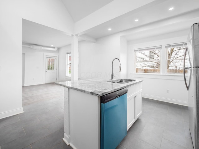 kitchen with appliances with stainless steel finishes, white cabinetry, sink, light stone countertops, and a center island with sink