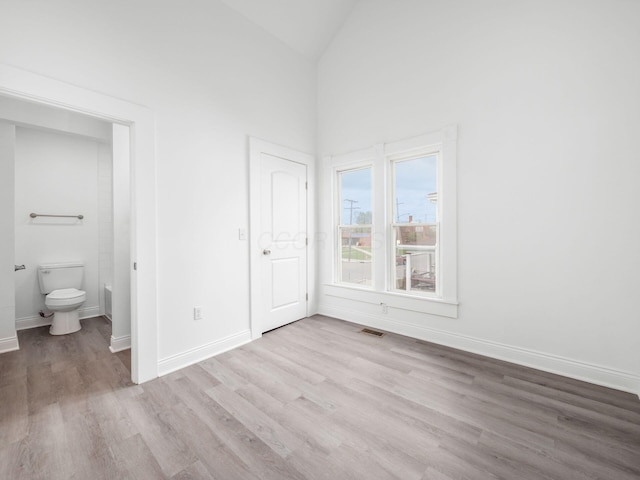 unfurnished bedroom with high vaulted ceiling, light hardwood / wood-style floors, and ensuite bath