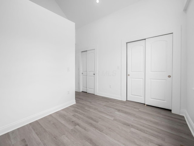 unfurnished bedroom featuring multiple closets, high vaulted ceiling, and light hardwood / wood-style flooring