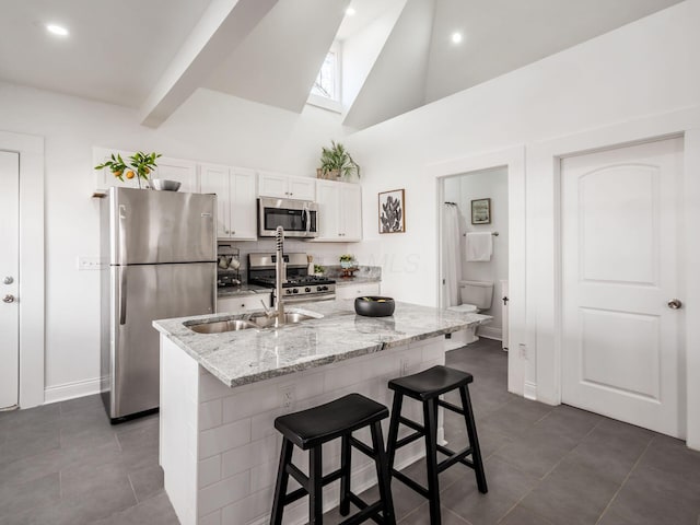 kitchen featuring a breakfast bar, stainless steel appliances, light stone countertops, a kitchen island with sink, and white cabinets