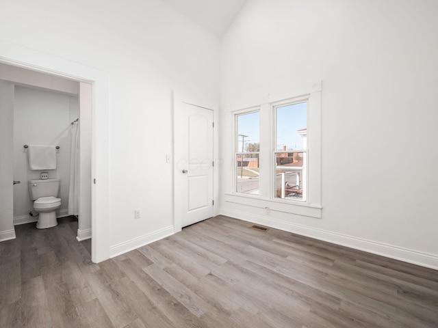 unfurnished bedroom with ensuite bath, vaulted ceiling, and light hardwood / wood-style flooring