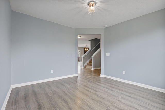 empty room featuring a chandelier, light hardwood / wood-style flooring, and a textured ceiling