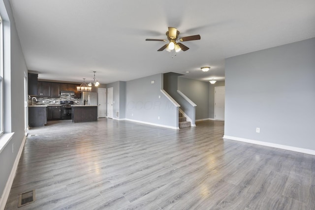 unfurnished living room featuring hardwood / wood-style floors, ceiling fan with notable chandelier, and sink