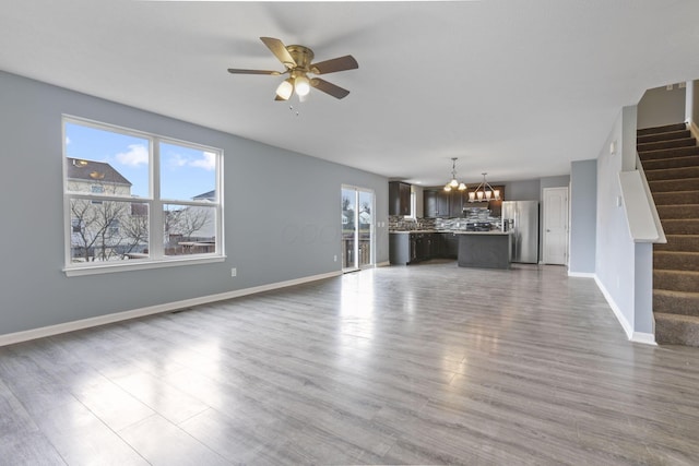 unfurnished living room featuring wood-type flooring and ceiling fan with notable chandelier