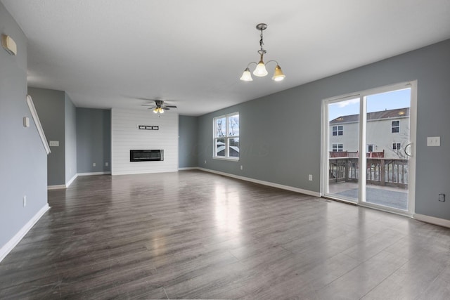 unfurnished living room featuring a large fireplace, ceiling fan with notable chandelier, and dark wood-type flooring