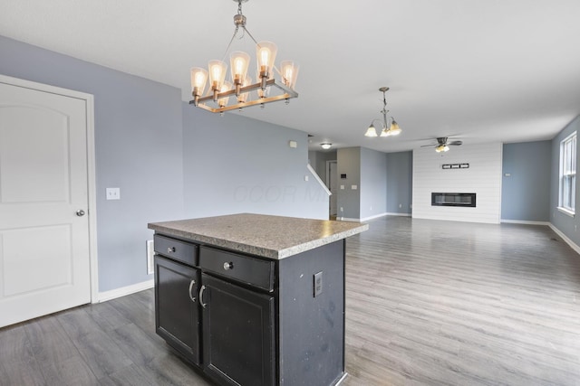 kitchen with hanging light fixtures, a center island, a fireplace, dark hardwood / wood-style flooring, and ceiling fan with notable chandelier