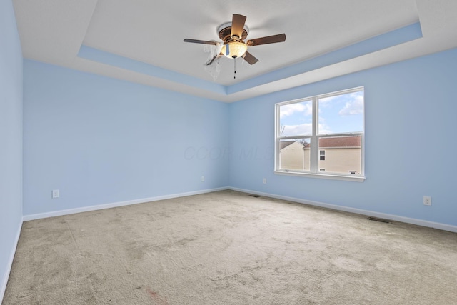 carpeted empty room featuring ceiling fan and a raised ceiling