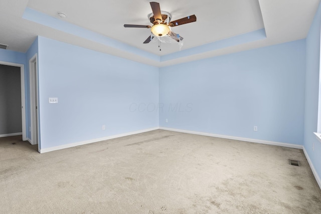 spare room with a raised ceiling, light colored carpet, and ceiling fan