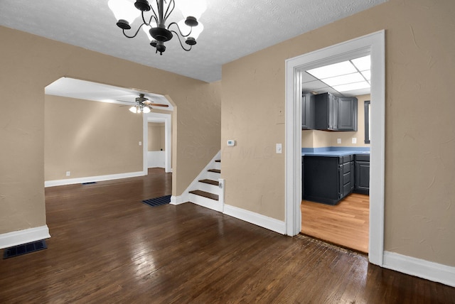 unfurnished dining area with visible vents, stairway, dark wood-style floors, ceiling fan with notable chandelier, and arched walkways