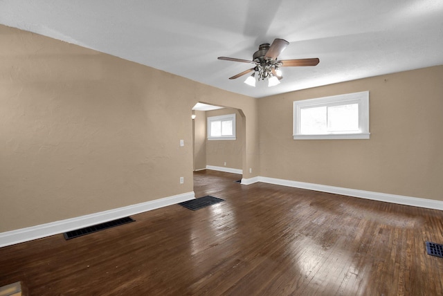 empty room featuring visible vents, a ceiling fan, hardwood / wood-style floors, arched walkways, and baseboards