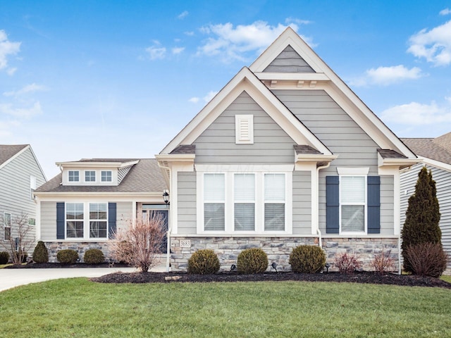 craftsman inspired home with a shingled roof, stone siding, and a front lawn