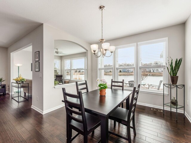 dining space featuring arched walkways, ceiling fan with notable chandelier, wood-type flooring, and baseboards