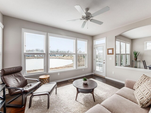 living area featuring arched walkways, ceiling fan, dark wood-type flooring, visible vents, and baseboards