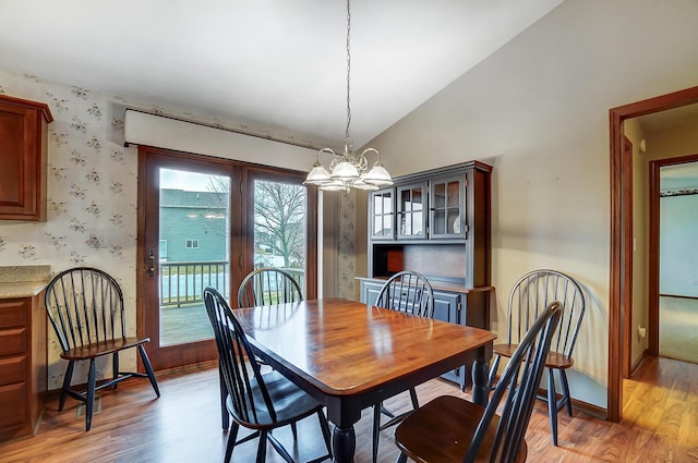 dining area with light wood-type flooring, wallpapered walls, a chandelier, and vaulted ceiling