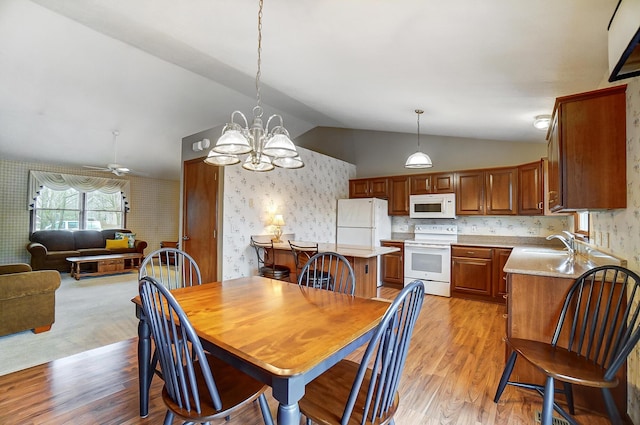 dining space with lofted ceiling, light wood-style floors, a chandelier, and wallpapered walls