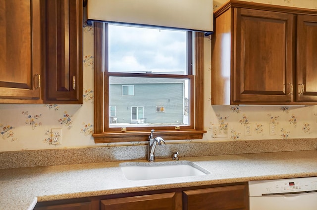 kitchen featuring dishwasher, light stone counters, a sink, and brown cabinets