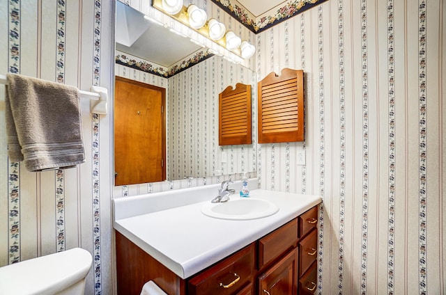 bathroom with toilet, wallpapered walls, and vanity