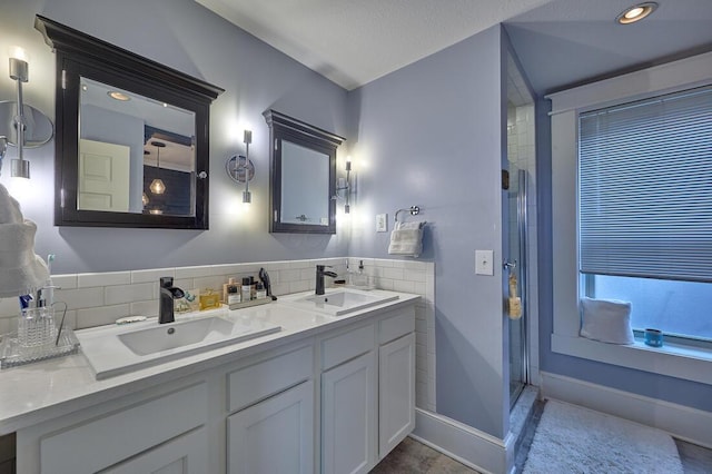 full bath featuring baseboards, a sink, double vanity, and a shower stall