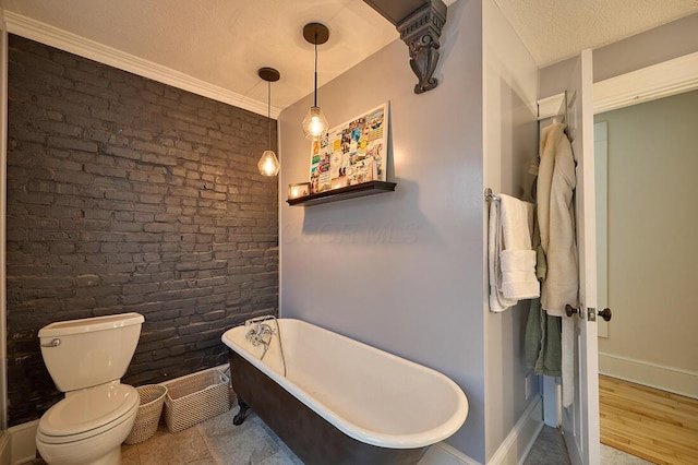 full bath with a freestanding bath, baseboards, toilet, and brick wall