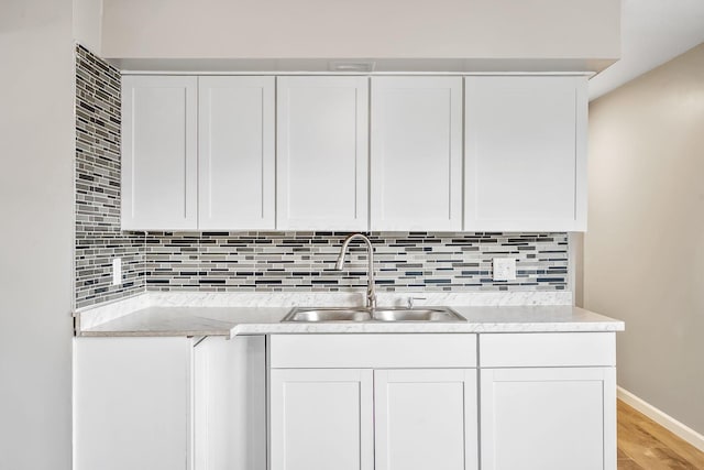 kitchen featuring sink, light stone counters, light hardwood / wood-style floors, white cabinets, and decorative backsplash