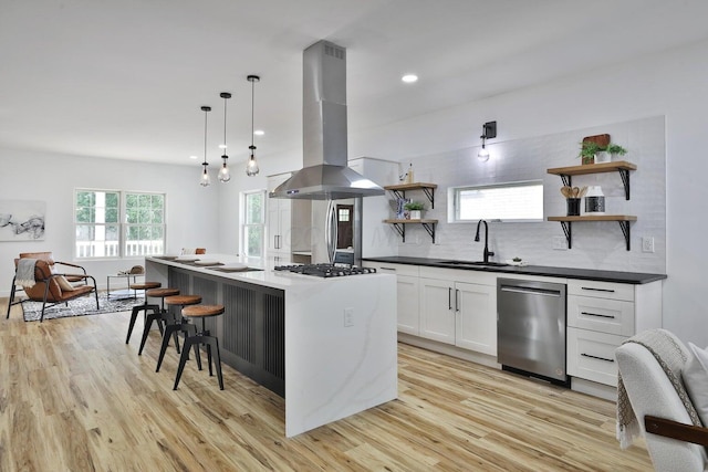 kitchen with sink, decorative light fixtures, appliances with stainless steel finishes, a kitchen island, and island exhaust hood