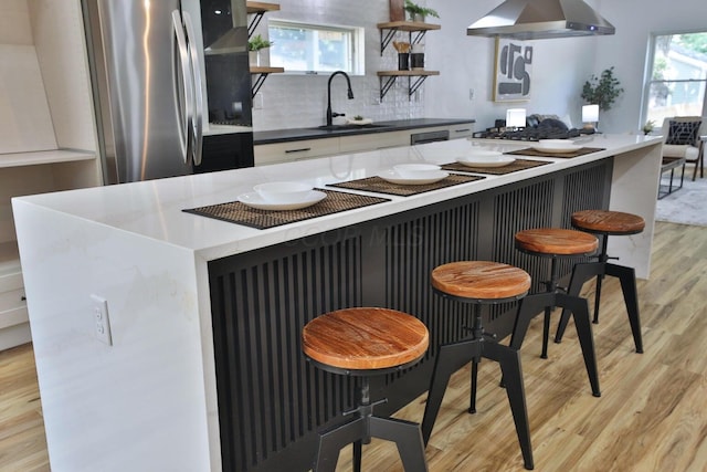 kitchen featuring a kitchen bar, sink, tasteful backsplash, light hardwood / wood-style flooring, and stainless steel appliances