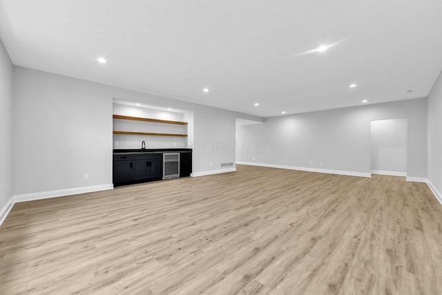 unfurnished living room with wine cooler, a textured ceiling, indoor wet bar, and light wood-type flooring