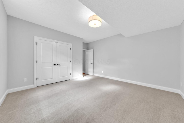 unfurnished bedroom featuring light colored carpet, a textured ceiling, and a closet