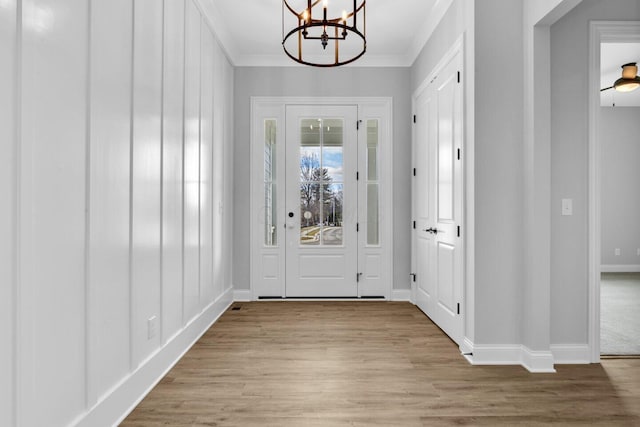 entryway with ornamental molding, light hardwood / wood-style floors, and a chandelier