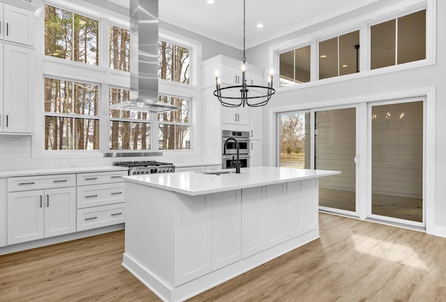 kitchen with island range hood, an island with sink, white cabinets, decorative backsplash, and light wood-type flooring