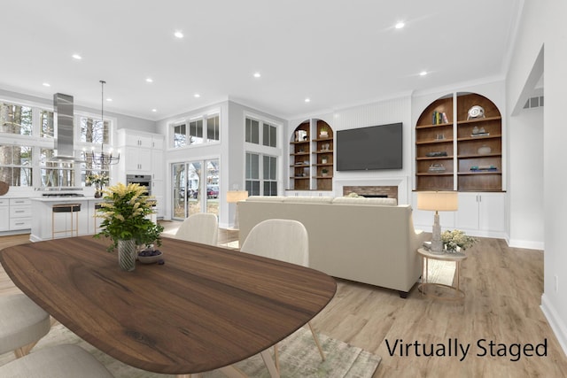 dining room featuring an inviting chandelier, ornamental molding, built in features, and light wood-type flooring