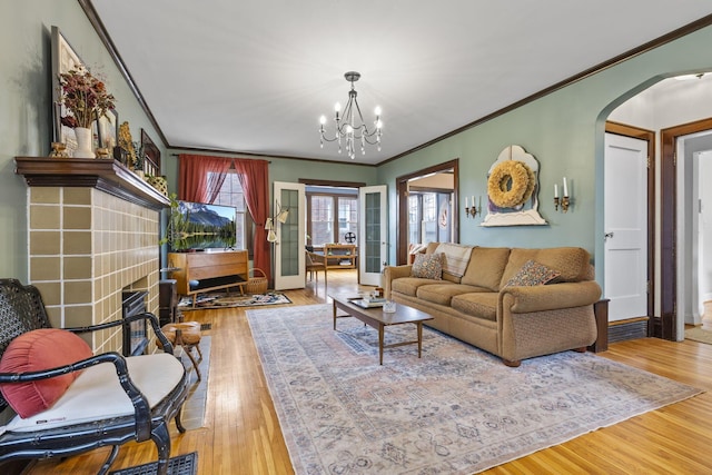 living room with an inviting chandelier, ornamental molding, wood-type flooring, and a tile fireplace